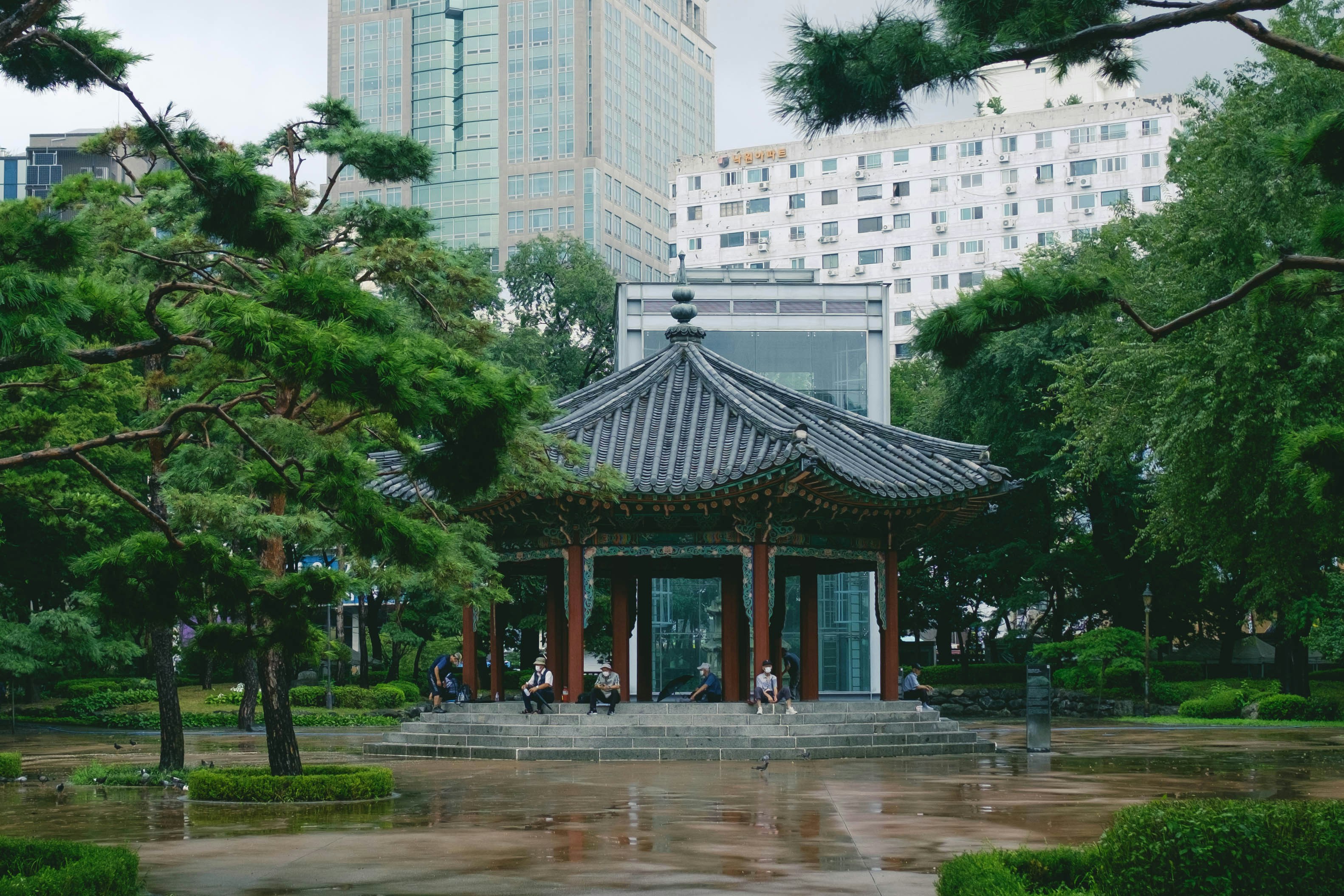 a small pavilion in a park with tall buildings in the background