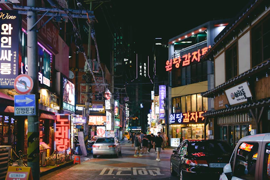 A lively group of travelers dressed in K-pop inspired outfits exploring neon-lit streets of Seoul at night.