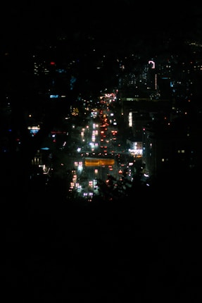 Nighttime cityscape with illuminated streets and buildings, featuring bright lights and a busy atmosphere.