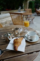 a wooden table topped with a cup of coffee and a croissant