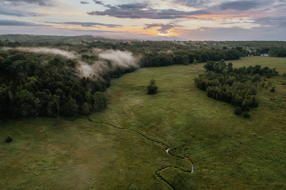 an aerial view of a field with trees and clouds