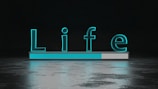 The word 'Life' is displayed in large, glowing teal letters above a horizontal progress bar that is partially filled. The background is dark with a reflective surface below the text and bar, creating a sense of depth and modernity.