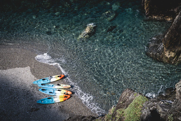 Colorful kayaks resting on a beach with rolling waves and a bright sun overhead.