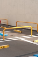 A parking area with yellow metal barriers and painted white lines on the asphalt. Japanese warning signs are positioned near the barriers. The backdrop is a plain concrete wall.