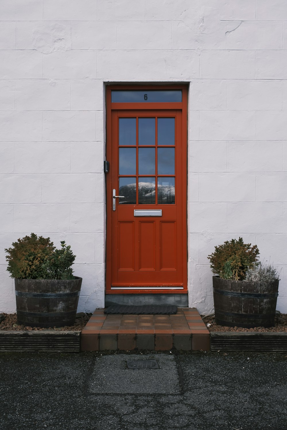 a red door and two planters on the side of a white building