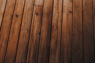 Wooden planks arranged in parallel, displaying a natural grain pattern with knots and varying shades of brown.