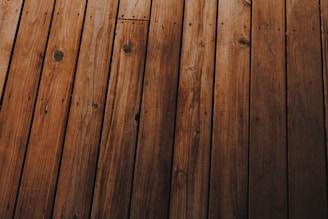 Wooden planks arranged in parallel, displaying a natural grain pattern with knots and varying shades of brown.