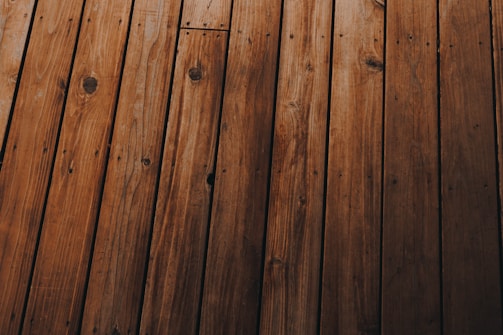 Wooden planks arranged in parallel, displaying a natural grain pattern with knots and varying shades of brown.
