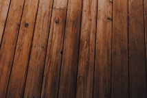 Wooden planks arranged in parallel, displaying a natural grain pattern with knots and varying shades of brown.