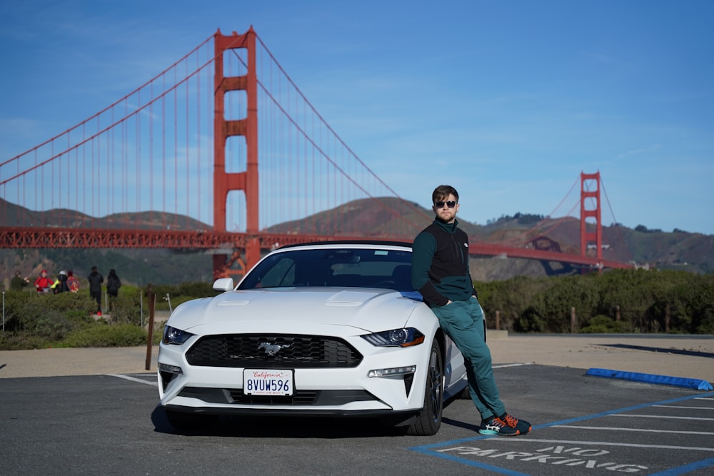 a man standing next to a white car in front of the golden gate bridge