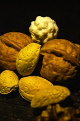 A close-up arrangement of shelled nuts, including walnuts and almonds, with a small piece of white popcorn positioned on top. The surface they rest on is dark, enhancing the warm tones of the nuts.