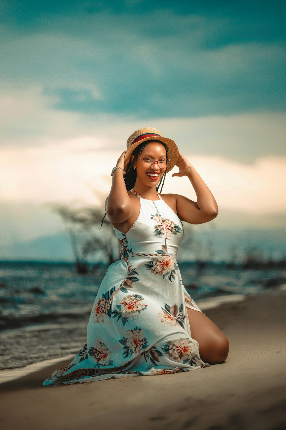 a woman in a dress and hat sitting on the beach