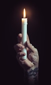 Close-up of a weathered hand holding a small, flickering candle inside a sewer.