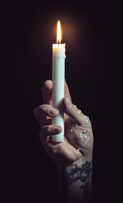 Close-up of a weathered hand holding a small, flickering candle inside a sewer.