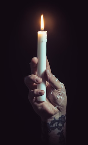 A close-up of a weathered hand holding a small, flickering candle inside a sewer chamber.