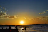 A serene coastal landscape at sunset with silhouettes of people walking along the shore.
