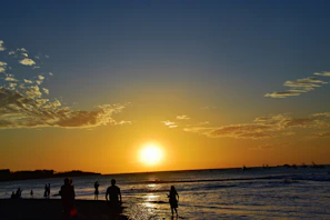 A serene coastal landscape at sunset with silhouettes of people walking along the shore.