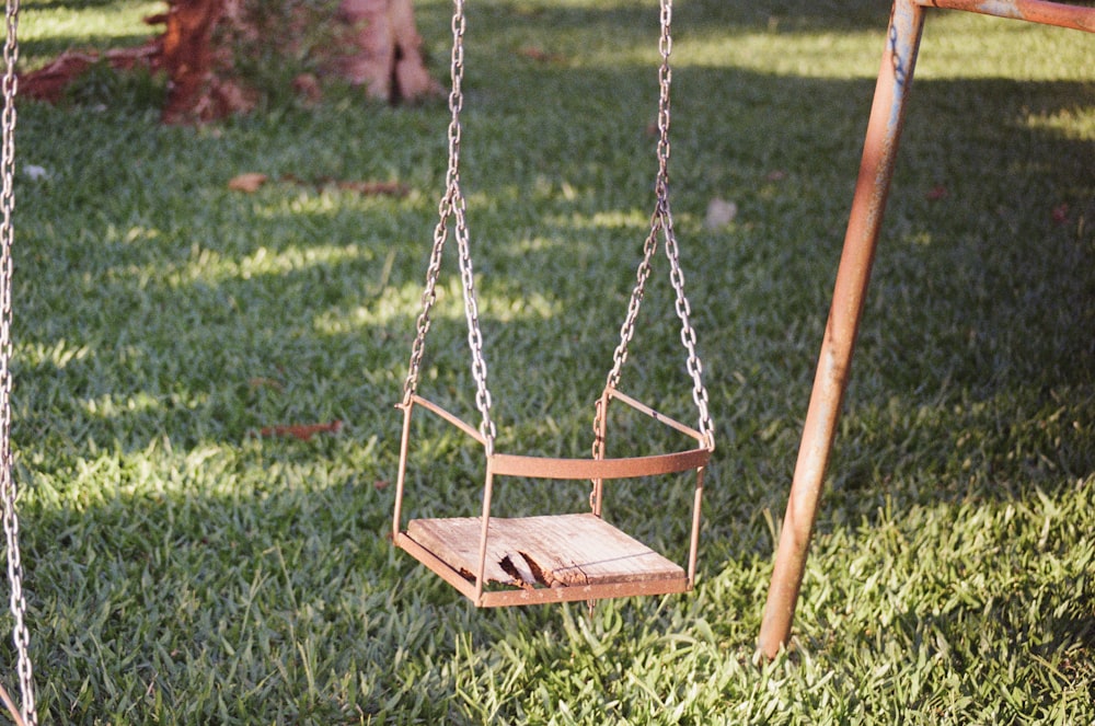 a wooden swing in the grass near a tree