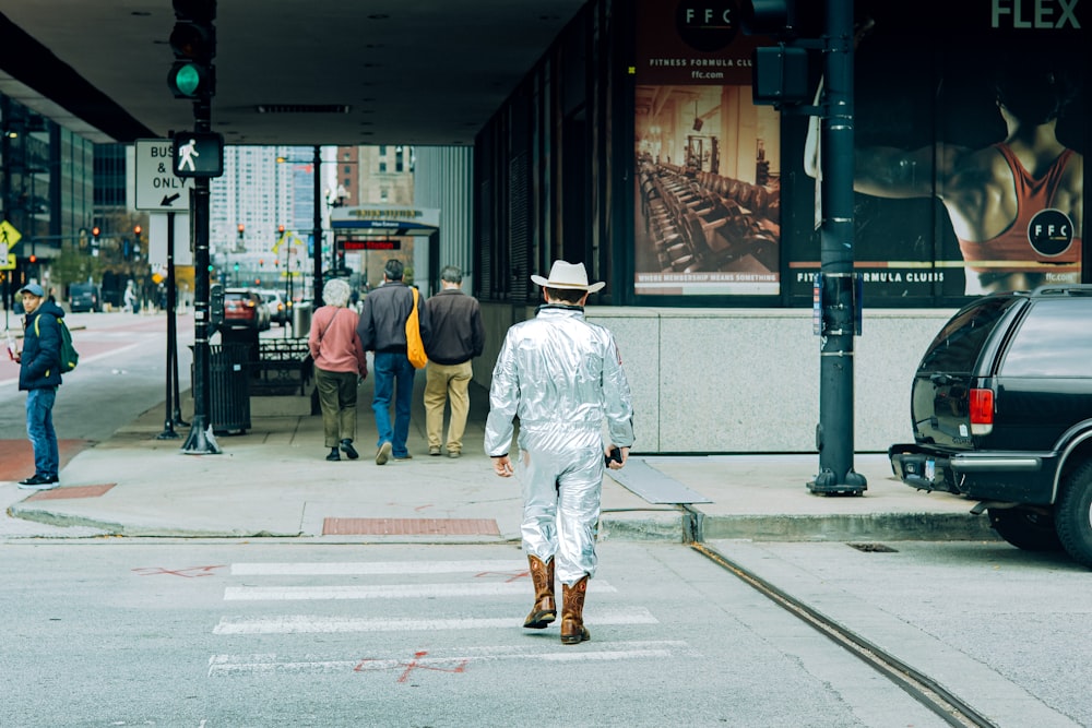 a man in a white suit and hat crossing a street
