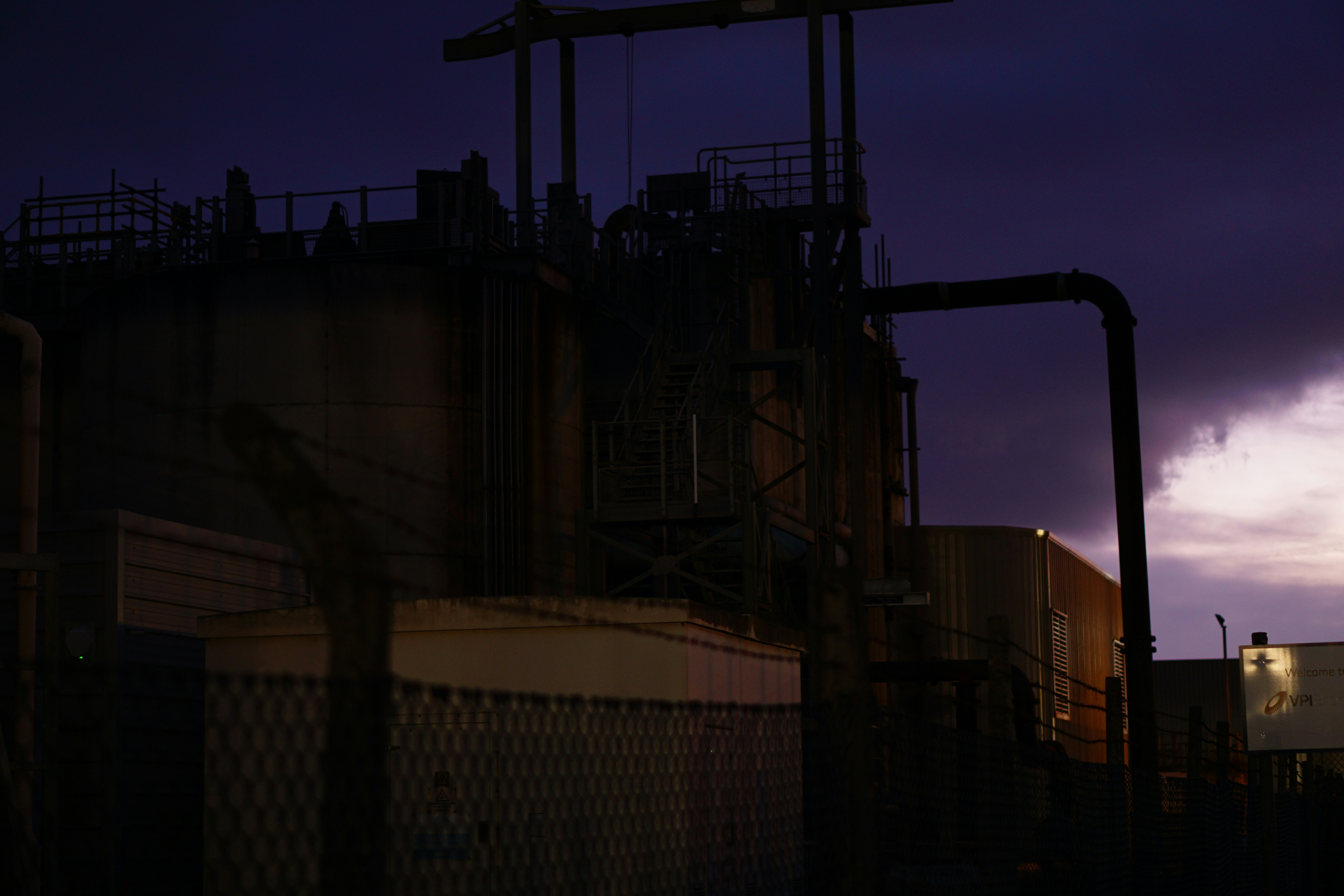 Full modular industrial process plant exterior at dusk, dramatic sky, steel structures silhouetted, low-key industrial atmosphere