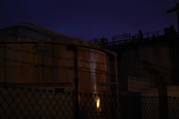 Industrial-scale sulphur storage tanks illuminated by warm brass-toned lights at dusk.