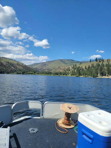 A compact day-cooler resting on a fishing boat deck with cold drinks inside and a scenic lake view.