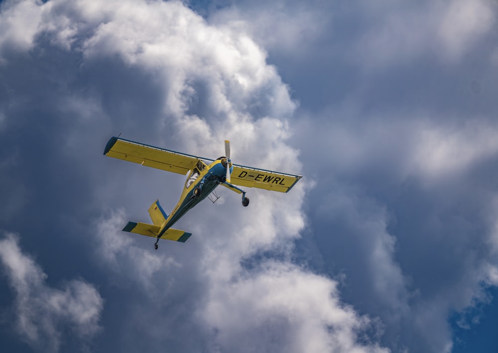 a yellow and blue plane flying through a cloudy sky