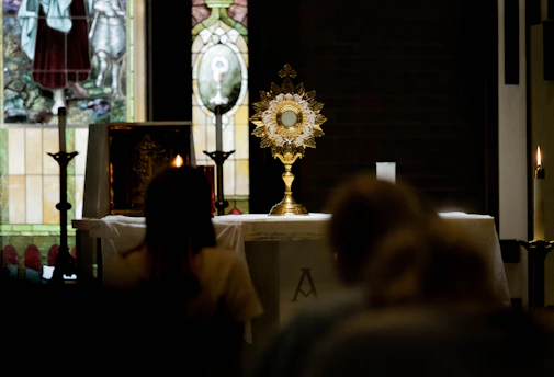 A golden monstrance glowing softly against a dark royal purple velvet backdrop inside a cathedral.
