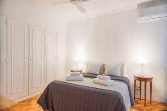 A friendly cleaner in uniform carefully making a bed in a bright, cozy rental room.