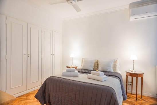 A friendly cleaner in uniform carefully making a bed in a bright, cozy rental room.