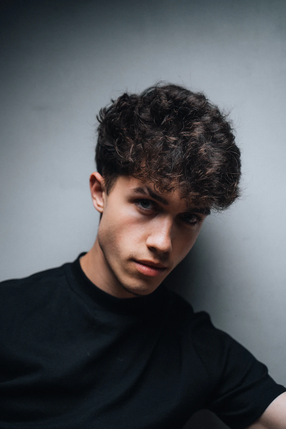 Young man with curly hair smiles directly at the camera in a plain white room