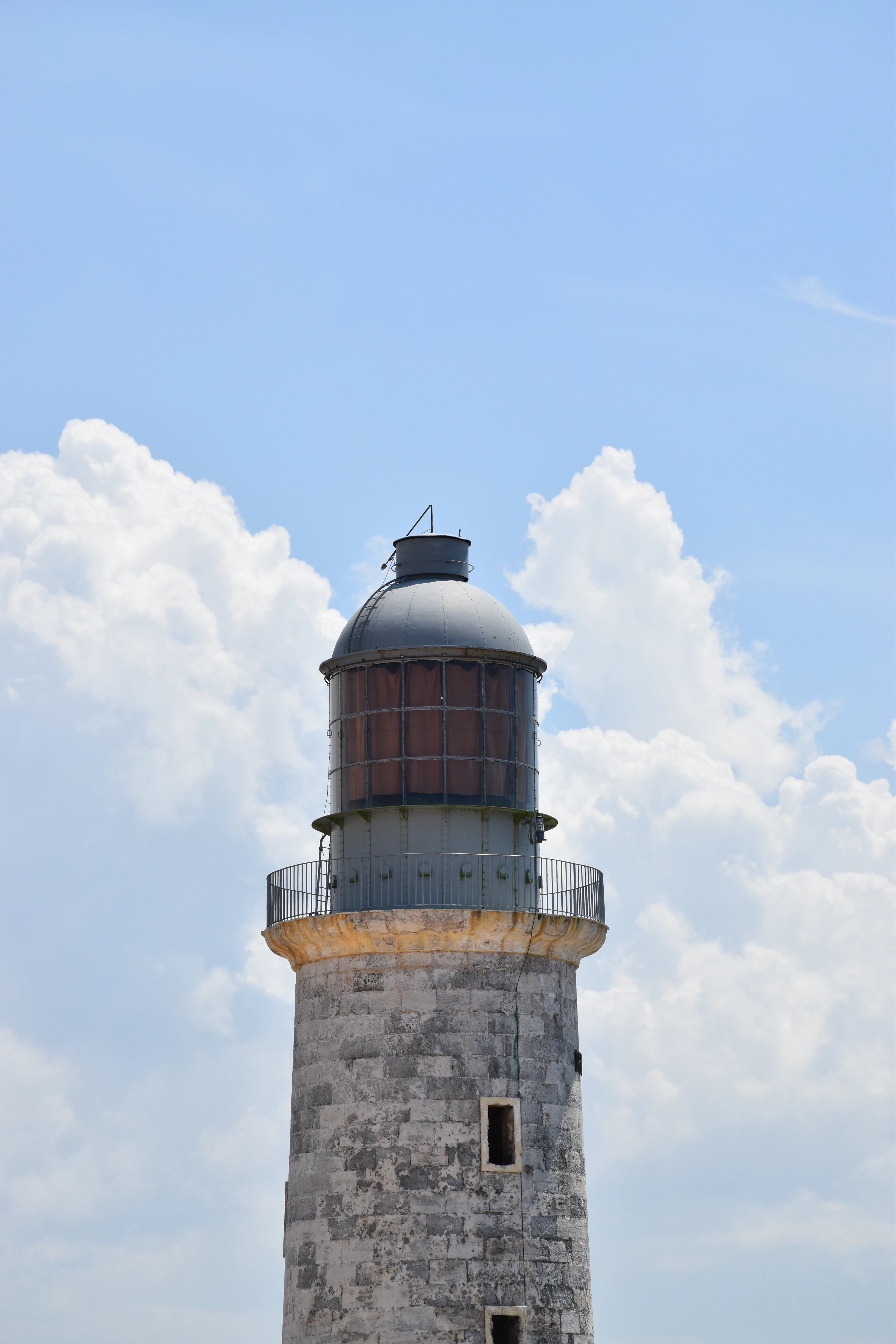A stone lighthouse tower rises against a sky filled with dramatic white clouds.