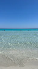 Crystal clear turquoise waters gently lapping a sandy beach in Ayvalik under bright sunlight.