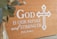 A wooden plaque featuring the phrase 'God is our refuge and strength' from Psalm 46:1 is displayed, with a decorative cross design beside the text. A blurred green plant is visible on the left in a glass vase.