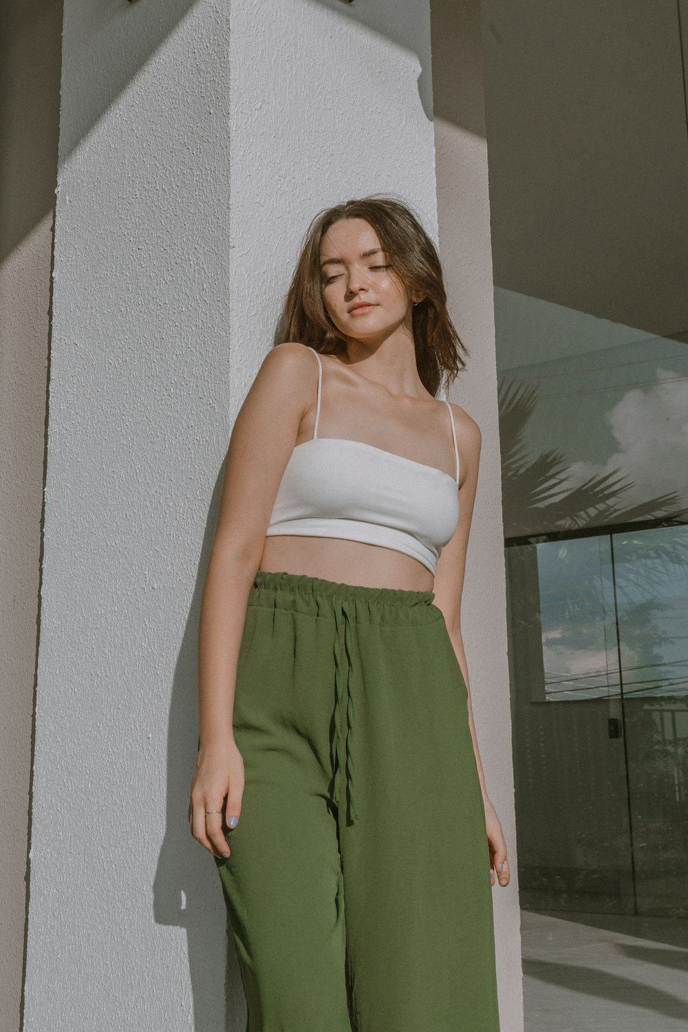 a woman leaning against a wall wearing green pants