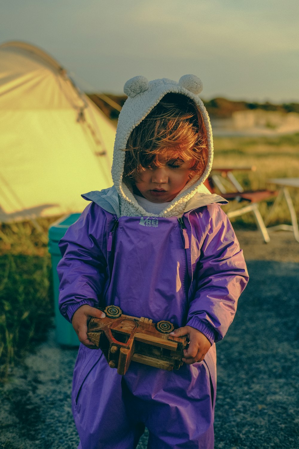 a young child in a purple rain suit holding a piece of wood