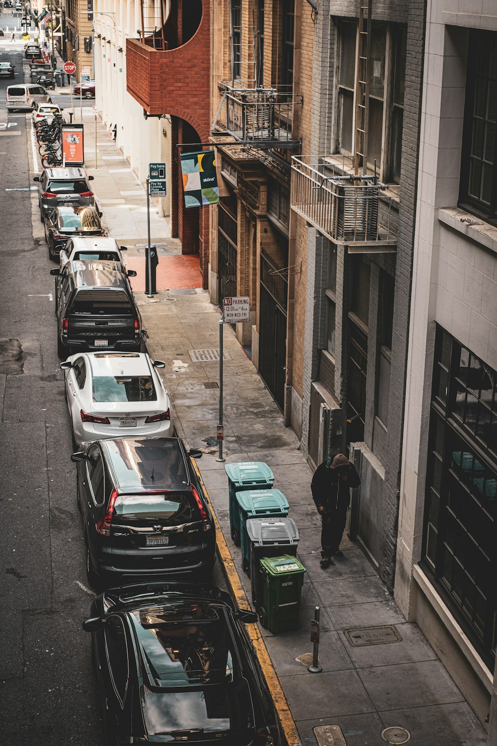 a man walking down a street next to a row of parked cars