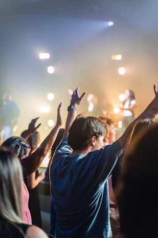 Crowd at a nighttime street concert, hands raised, illuminated by golden stage lights.