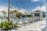 A luxurious outdoor swimming pool area surrounded by numerous reclining chairs, palm trees, and a modern building in the background. The sky is clear with a few clouds visible. The setting conveys a tranquil and inviting atmosphere, ideal for relaxation and leisure.