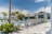 A luxurious outdoor swimming pool area surrounded by numerous reclining chairs, palm trees, and a modern building in the background. The sky is clear with a few clouds visible. The setting conveys a tranquil and inviting atmosphere, ideal for relaxation and leisure.