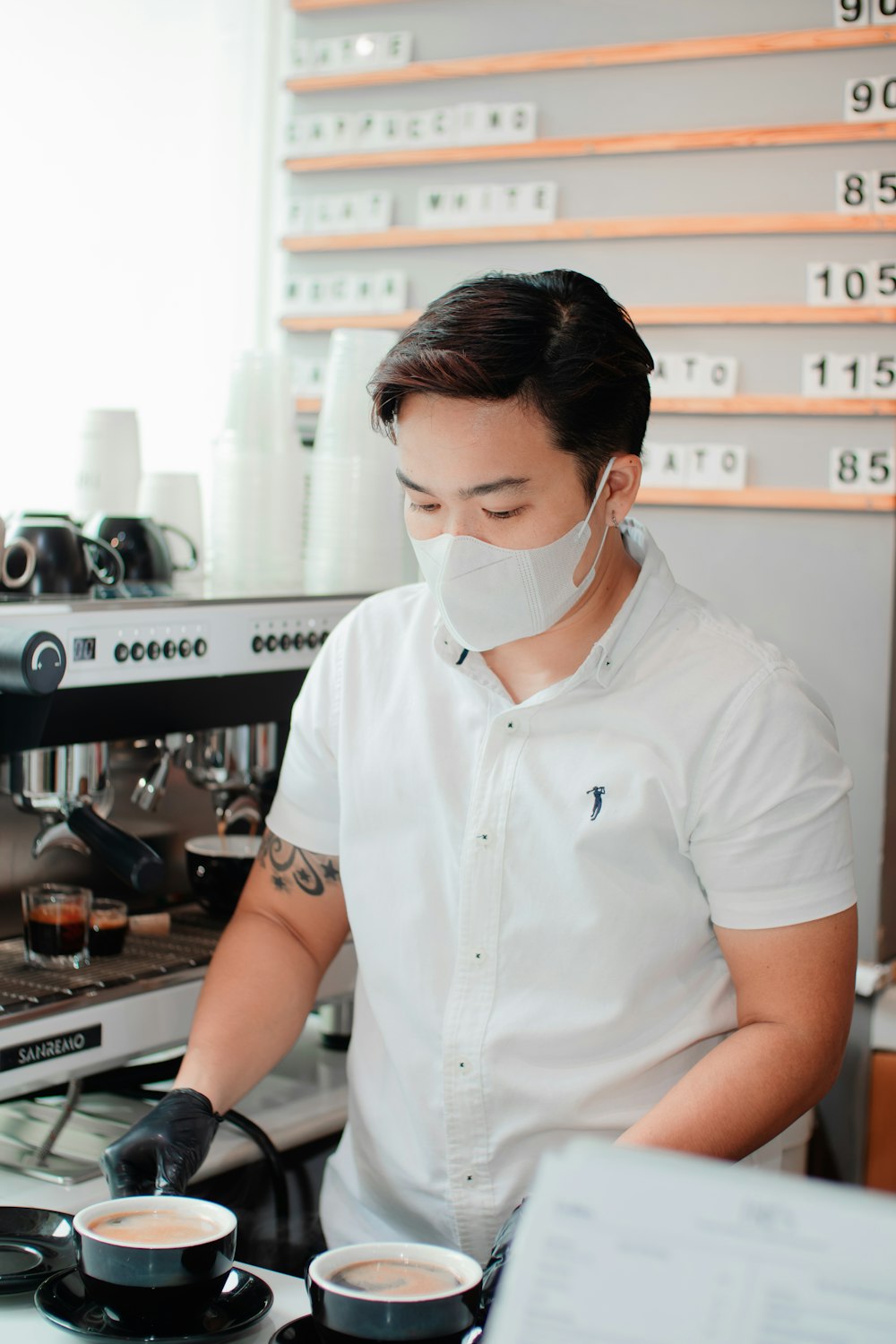 a man in a white shirt and a face mask is making a cup of coffee