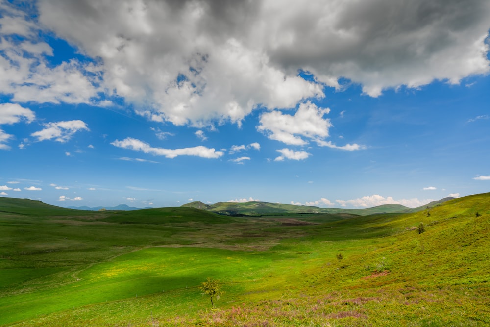 a green field with hills and clouds in the background