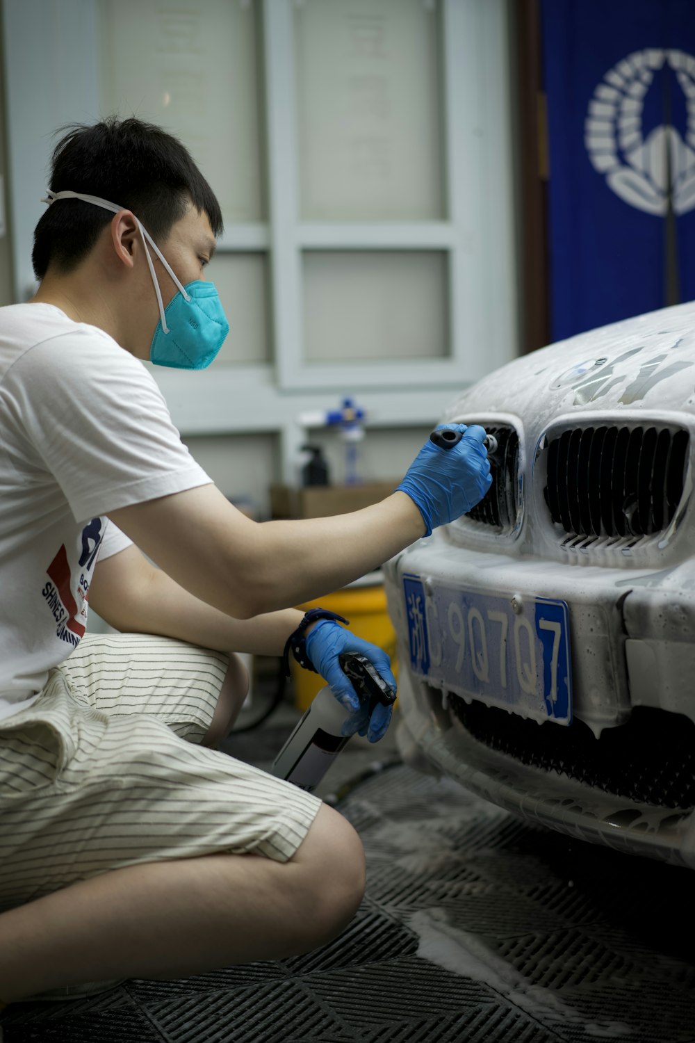a man wearing a face mask and gloves waxing a car