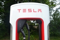 Close-up of a modern EV charging station with a Tesla plugged in, surrounded by greenery.