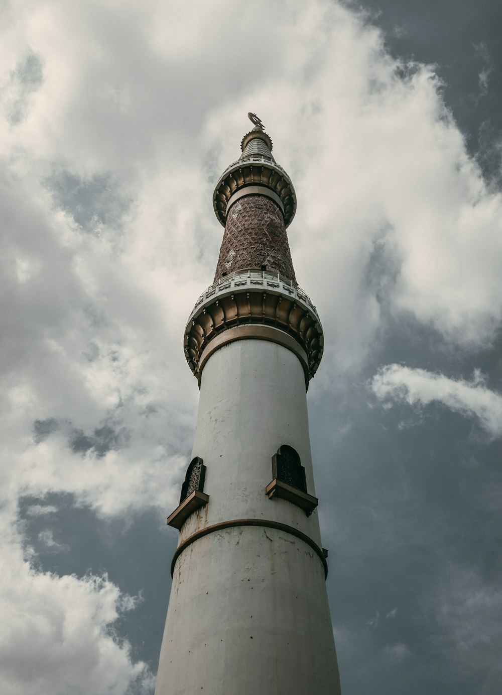 a tall white and brown lighthouse under a cloudy sky