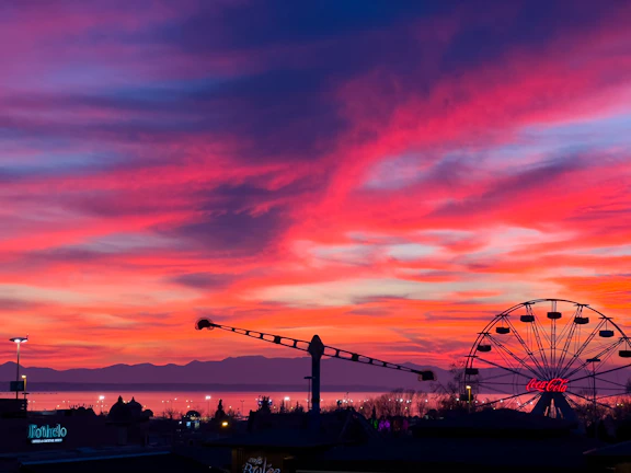 Sunset casting warm hues over a bustling amusement park with colorful rides.