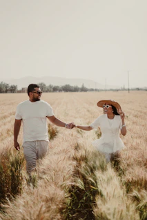 A sunlit couple walking hand in hand through a golden wheat field at sunset.