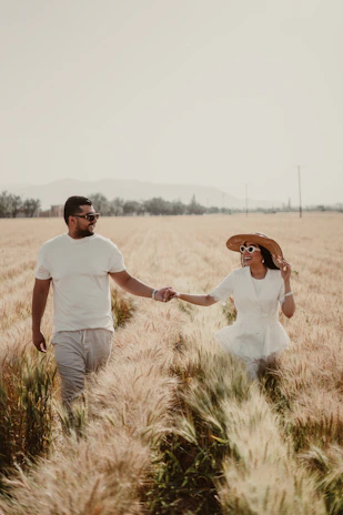 A sunlit couple walking hand in hand through a golden wheat field at sunset.