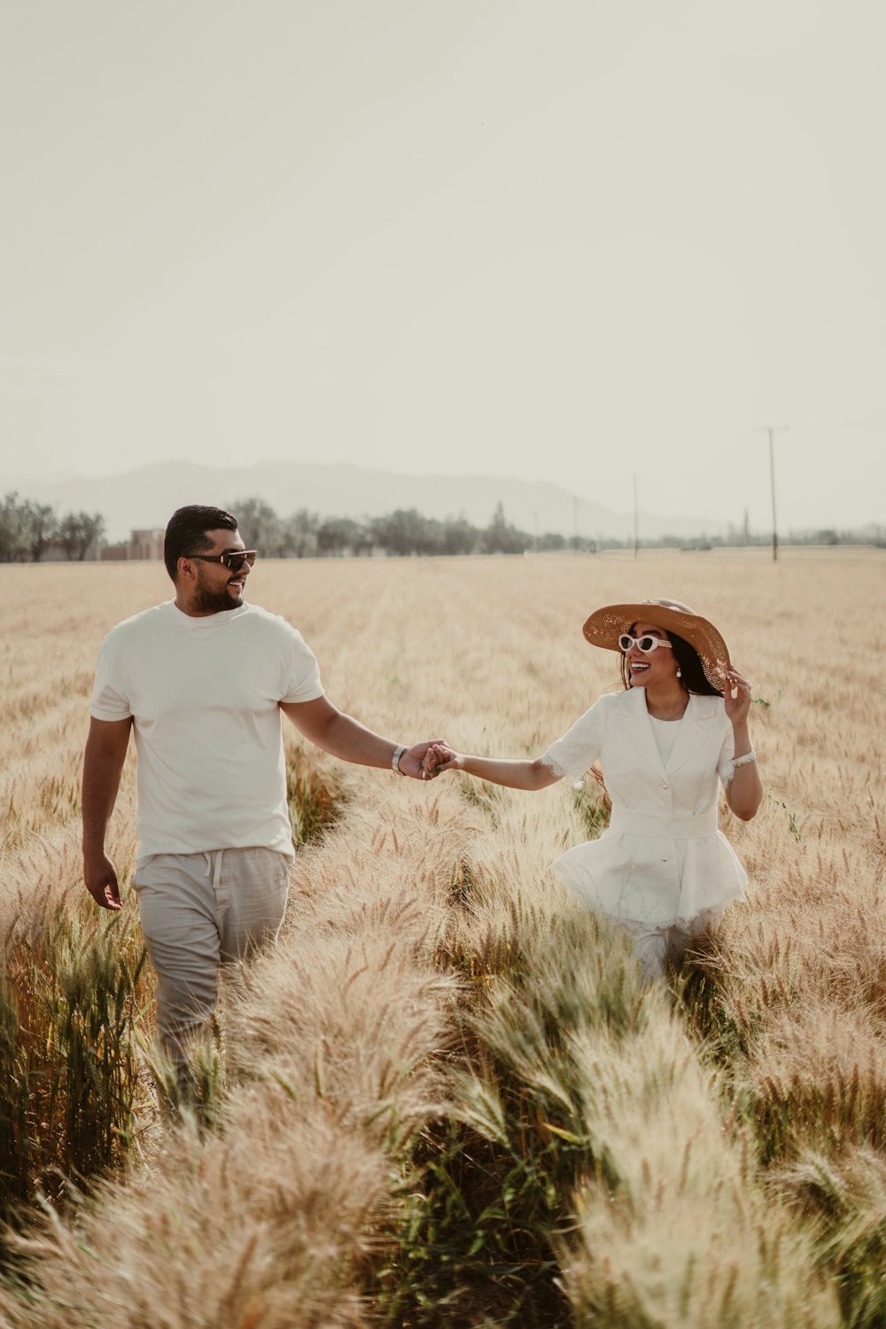 a man and a woman walking through a field holding hands