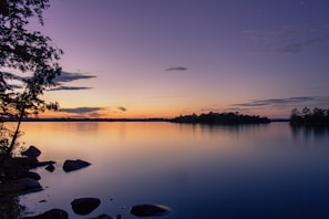 A serene lakeside view at sunset with calm waters reflecting the vibrant sky